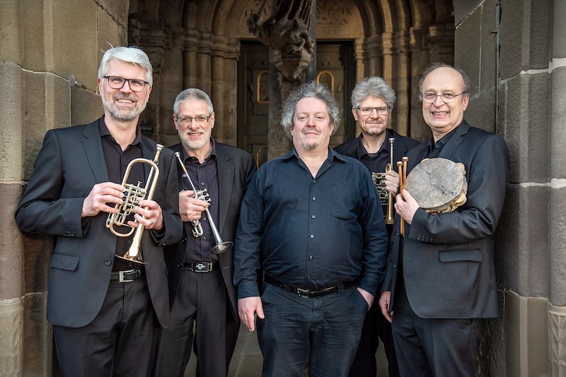Fünf Männer in schwarzen Anzügen stehen vor einem historischen Gebäude. Zwei halten Trompeten, einer eine Trommel. Sie lächeln in die Kamera., © Konzertbüro Joachim Jung Fünf Männer in schwarzen Anzügen stehen vor einem historischen Gebäude. Zwei halten Trompeten, einer eine Trommel. Sie lächeln in die Kamera., © Konzertbüro Joachim Jung