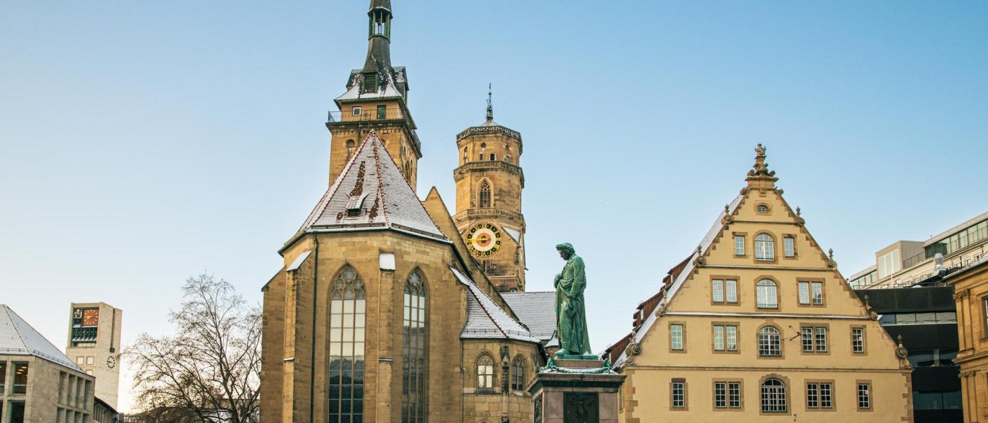 Die Stiftskirche in Stuttgart mit schneebedecktem Dach und einer Statue im Vordergrund. Der Himmel ist klar und blau., &copy; Stuttgart-Marketing GmbH, Sarah Schmid
