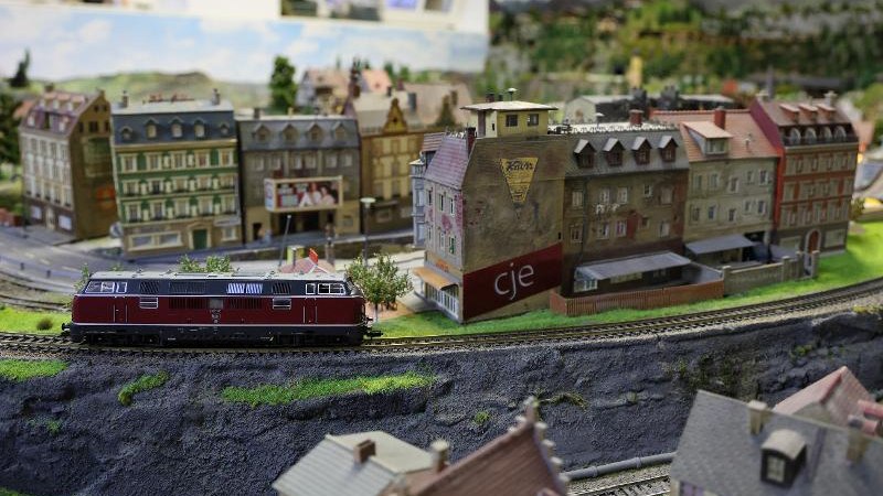 Eine detaillierte Modellbahnlandschaft mit einem roten Zug und Gebäuden. Die Szene zeigt eine Stadt mit Straßen und Häusern im Miniaturformat., © Backnang Eine detaillierte Modellbahnlandschaft mit einem roten Zug und Gebäuden. Die Szene zeigt eine Stadt mit Straßen und Häusern im Miniaturformat., © Backnang