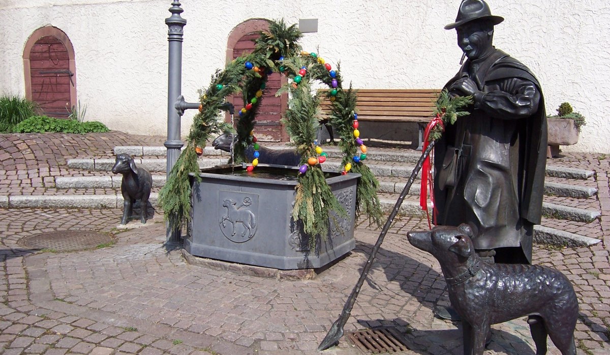 Ein Brunnen in Schafhausen, geschmückt mit Osterdekoration. Figuren eines Hirten, eines Hundes und eines Schafs sind zu sehen., © Natur.Nah. Schönbuch & Heckengäu Ein Brunnen in Schafhausen, geschmückt mit Osterdekoration. Figuren eines Hirten, eines Hundes und eines Schafs sind zu sehen., © Natur.Nah. Schönbuch & Heckengäu