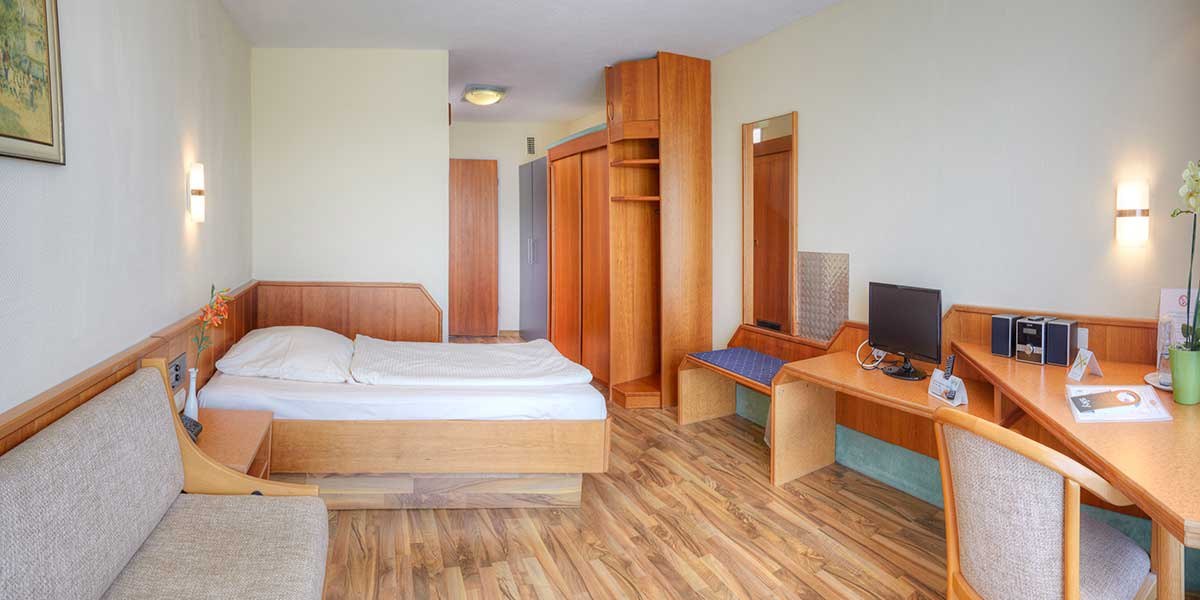 Ein gemütliches Einzelzimmer mit Holzmöbeln, Bett, Schreibtisch, Stuhl und Schrank. Helle Wände und Holzfußboden schaffen eine einladende Atmosphäre., © Kemnater Hof GmbH