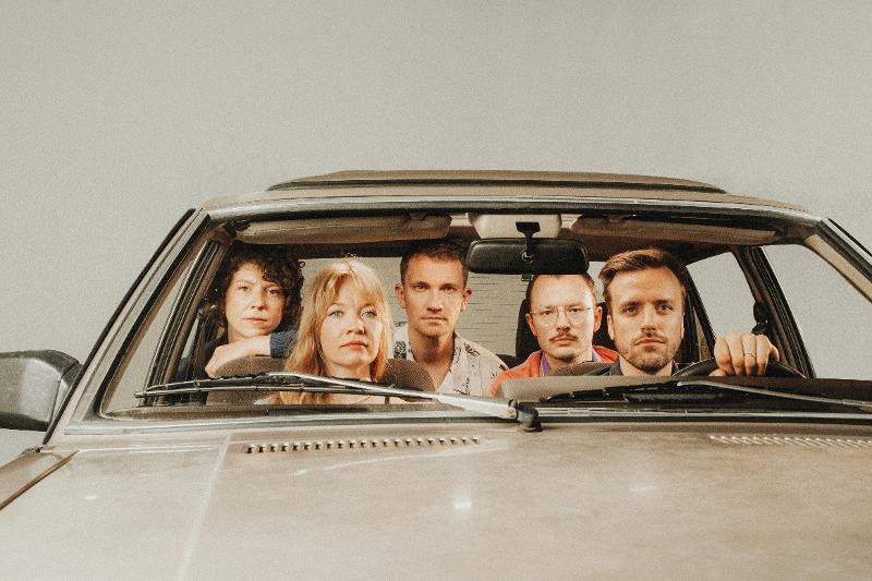 F&uuml;nf Personen sitzen in einem Auto und blicken ernst nach vorne. Die Szene wirkt inszeniert und k&uuml;nstlerisch., &copy; SKS Michael Russ GmbH