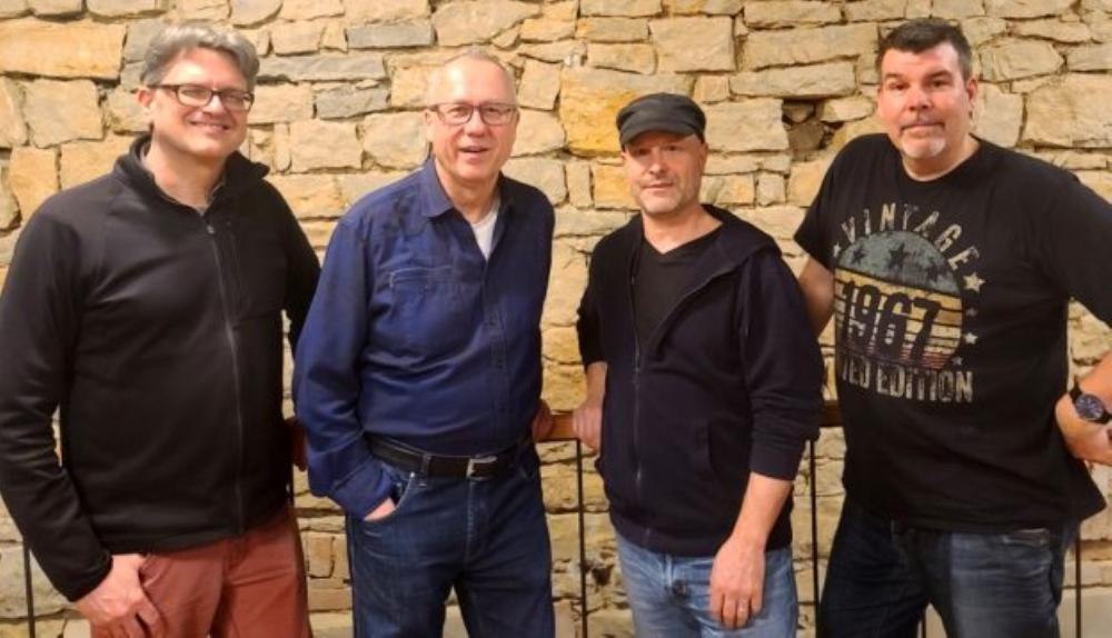 Vier M&auml;nner posieren l&auml;chelnd vor einer Steinmauer. Sie tragen l&auml;ssige Kleidung und wirken entspannt., &copy; Foto Uli Binetsch