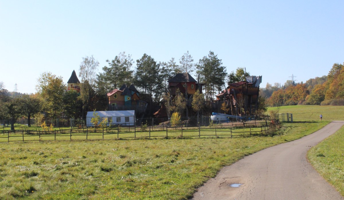 Ein Baumhaushotel mit bunten Häusern in einer ländlichen Landschaft, umgeben von Bäumen und Wiesen. Ein Weg führt am Hotel vorbei., © Natur.Nah. Schönbuch & Heckengäu Ein Baumhaushotel mit bunten Häusern in einer ländlichen Landschaft, umgeben von Bäumen und Wiesen. Ein Weg führt am Hotel vorbei., © Natur.Nah. Schönbuch & Heckengäu