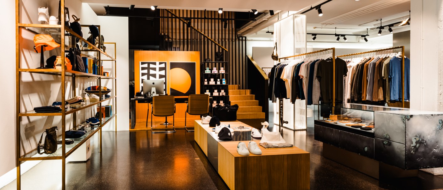 Modernes Herrenbekleidungsgeschäft mit stilvoller Einrichtung, Regalen voller Kleidung und Accessoires. Einladende Atmosphäre mit warmem Licht., © Bungalow