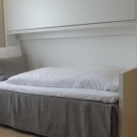 Ein Einzelbett mit weißer Bettwäsche und grauem Rock steht in einem Zimmer. Ein Etagenbett ist in die Wand eingeklappt., © Hotel am Engelberg