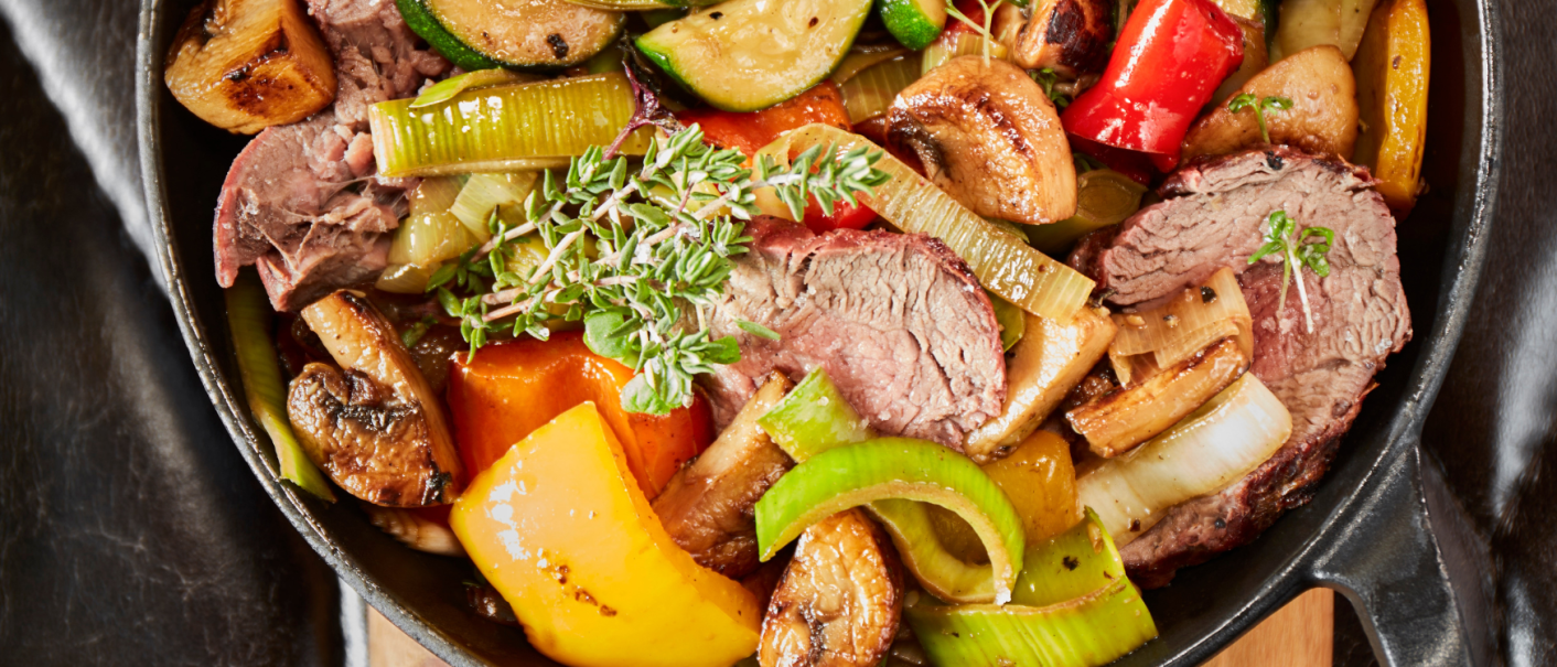 Pfanne mit gebratenem Fleisch, Zucchini, Paprika, Pilzen und Kräutern, serviert auf einem Holzbrett., © MAREDO