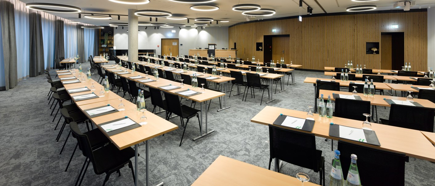 Moderner Konferenzraum mit Tischen, Stühlen und Notizblöcken, beleuchtet von runden Deckenleuchten. Wasserflaschen und Gläser sind auf den Tischen verteilt., © Holiday Inn Stuttgart Moderner Konferenzraum mit Tischen, Stühlen und Notizblöcken, beleuchtet von runden Deckenleuchten. Wasserflaschen und Gläser sind auf den Tischen verteilt., © Holiday Inn Stuttgart