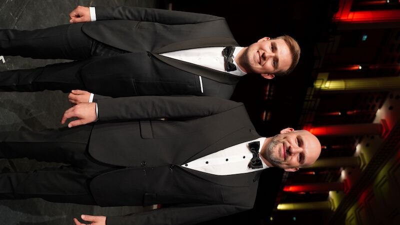 Zwei M&auml;nner in eleganten Anz&uuml;gen stehen auf einer B&uuml;hne. Der Hintergrund ist in warmen Farben beleuchtet, was eine festliche Atmosph&auml;re schafft., &copy; Touristik Bad Wildbad GmbH