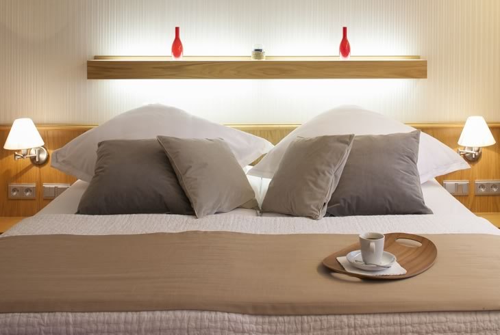Modernes Schlafzimmer mit Doppelbett, dekoriert mit Kissen und Tablett mit Tasse. Zwei rote Vasen auf einem Regal im Hintergrund., &copy; Hotel Drei Morgen