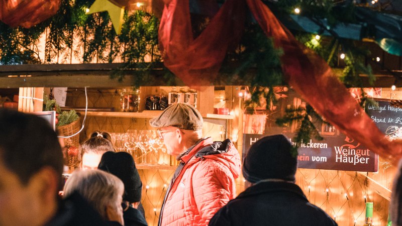Weihnachtsmarktstand mit Menschen, Lichterketten und festlicher Dekoration. Ein Mann in roter Jacke steht im Vordergrund., © Wirtschaftsförderung Sindelfingen GmbH Weihnachtsmarktstand mit Menschen, Lichterketten und festlicher Dekoration. Ein Mann in roter Jacke steht im Vordergrund., © Wirtschaftsförderung Sindelfingen GmbH