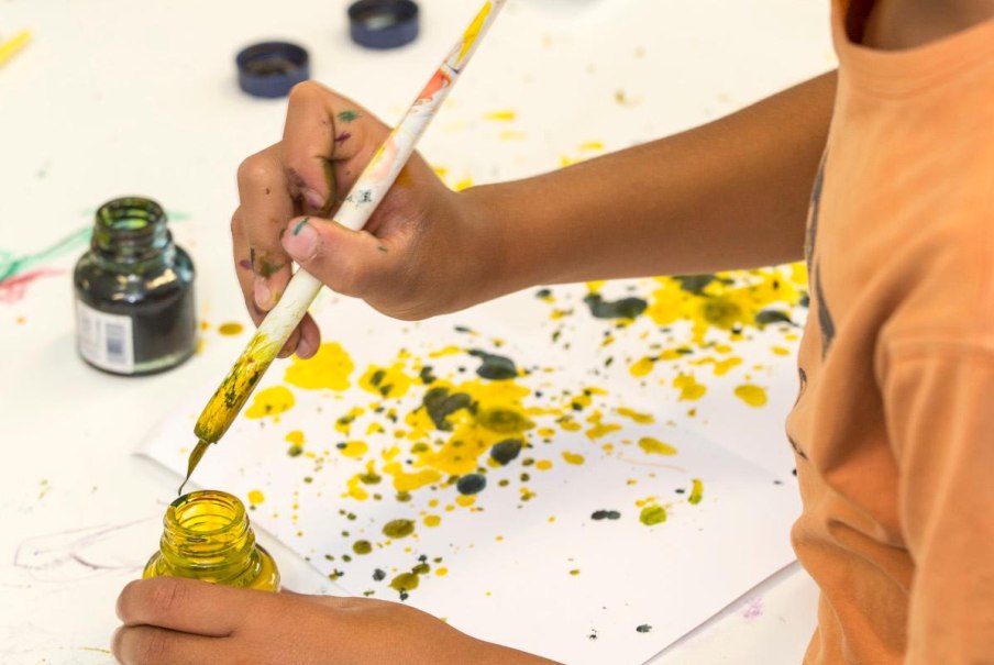 Ein Kind malt mit einem Pinsel und gelber Farbe auf Papier. Die H&auml;nde sind farbig verschmiert, und es gibt Farbspritzer auf dem Papier., &copy; Ludwigsburg Museum