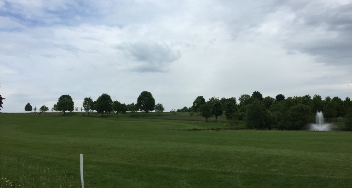 Ein weitl&auml;ufiger Golfplatz mit gr&uuml;ner Wiese, B&auml;umen und einem Springbrunnen im Hintergrund. Der Himmel ist bew&ouml;lkt., &copy; www.pro-cycl.de