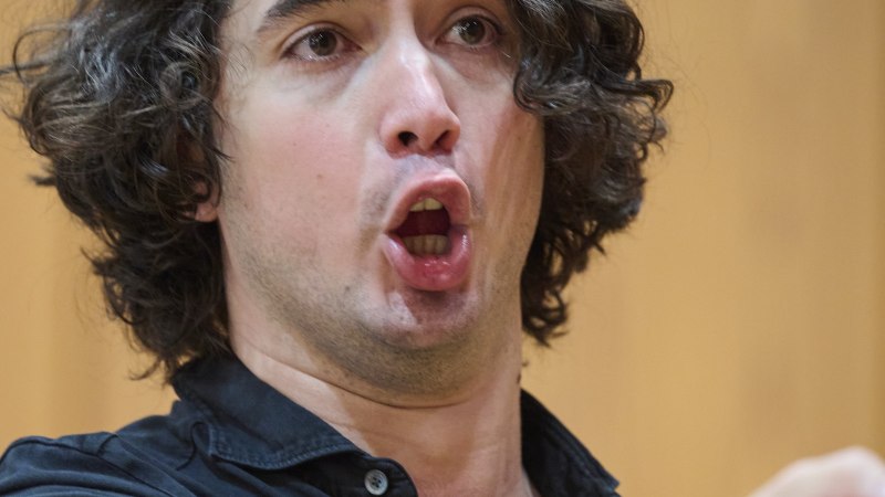 Ein Mann mit lockigem Haar singt leidenschaftlich und gestikuliert mit der Hand. Er tr&auml;gt ein schwarzes Hemd und steht vor einem unscharfen Hintergrund., &copy; www.peter-oppenlaender.de