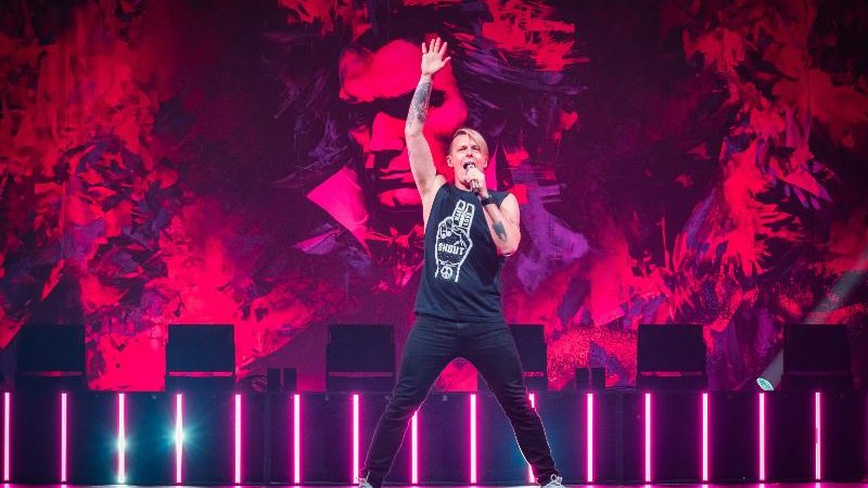 Ein Sänger performt auf einer Bühne mit rotem Hintergrund. Er trägt ein schwarzes Shirt und hebt eine Hand in die Luft., © Ludwigsburg