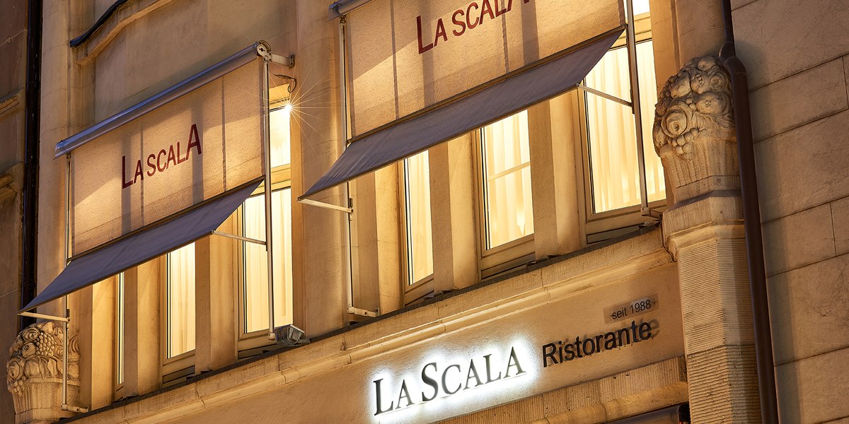 Beleuchtete Fassade des Restaurants La Scala in Stuttgart mit Markisen und dekorativen Säulen bei Nacht., © La Scala
