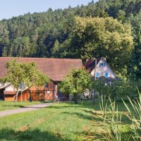 Ein Bauernhof mit Scheune und Wohnhaus, umgeben von Bäumen und Wiesen, vor einem bewaldeten Hügel., © Natur.Nah. Schönbuch & Heckengäu Ein Bauernhof mit Scheune und Wohnhaus, umgeben von Bäumen und Wiesen, vor einem bewaldeten Hügel., © Natur.Nah. Schönbuch & Heckengäu
