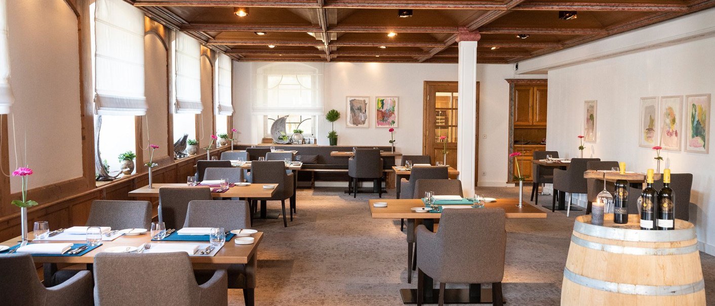 Elegantes Restaurant mit Holztischen, grauen Stühlen und einem Weinfass. Helle Fenster und moderne Kunst an den Wänden schaffen eine einladende Atmosphäre., © Schlosshotel Monrepos Elegantes Restaurant mit Holztischen, grauen Stühlen und einem Weinfass. Helle Fenster und moderne Kunst an den Wänden schaffen eine einladende Atmosphäre., © Schlosshotel Monrepos