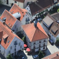Luftaufnahme eines Dorfes mit Fachwerkhäusern und roten Dächern. Im Zentrum ein Gebäude mit rotem Dach und Sonnenschirmen., © Hotel Gasthof Lamm