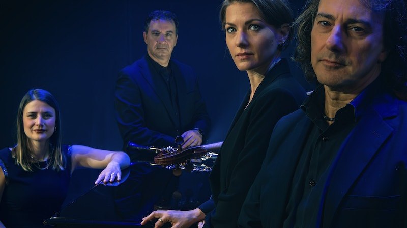 Vier Musiker in dunkler Kleidung posieren ernst vor einem dunklen Hintergrund. Sie stehen um ein Klavier herum., &copy; Buchhandlung Im Roten Haus