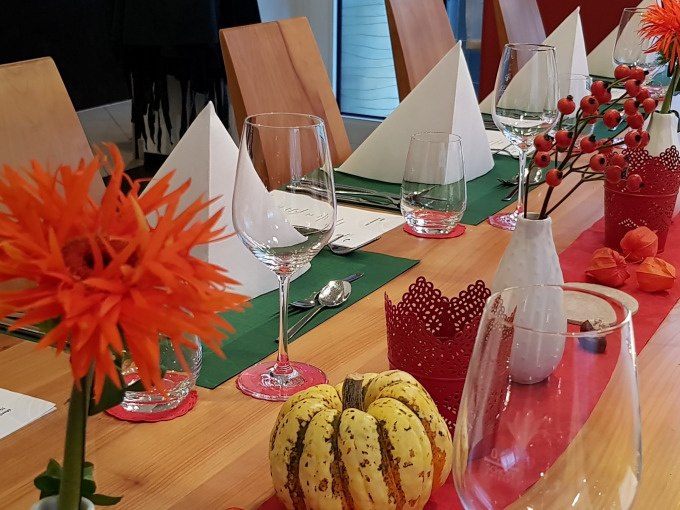 Ein festlich gedeckter Tisch mit Gl&auml;sern, wei&szlig;en Servietten, orangefarbenen Blumen und herbstlicher Dekoration in einem modernen Raum., &copy; Kultweine-Kochwelten-Kunst&uuml;cke - Kochschule Sonja Lenz