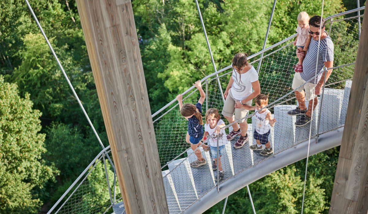 Eine Familie spaziert auf einem erhöhten Baumkronenpfad, umgeben von grünen Bäumen. Kinder und Erwachsene genießen die Aussicht., © Natur.Nah. Schönbuch & Heckengäu Eine Familie spaziert auf einem erhöhten Baumkronenpfad, umgeben von grünen Bäumen. Kinder und Erwachsene genießen die Aussicht., © Natur.Nah. Schönbuch & Heckengäu