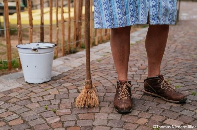 Beine einer Person in braunen Schuhen und blauem Rock, mit Besen und weißem Eimer auf Kopfsteinpflaster., © Stuttgart Marketing GmbH Beine einer Person in braunen Schuhen und blauem Rock, mit Besen und weißem Eimer auf Kopfsteinpflaster., © Stuttgart Marketing GmbH
