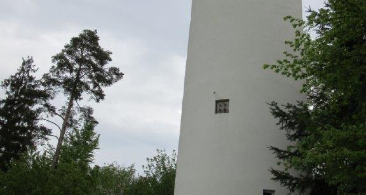 Ein weißer, runder Wasserturm in Jettingen steht vor einem bewölkten Himmel, umgeben von Bäumen und einer Bank mit Gießkanne., © Natur.Nah. Schönbuch & Heckengäu Ein weißer, runder Wasserturm in Jettingen steht vor einem bewölkten Himmel, umgeben von Bäumen und einer Bank mit Gießkanne., © Natur.Nah. Schönbuch & Heckengäu