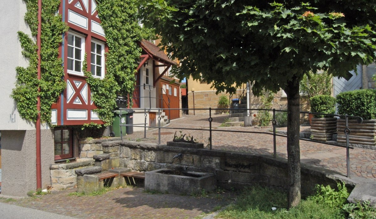 Fachwerkhaus mit Efeu bewachsen, daneben ein Baum und ein kleiner Brunnen in einer gepflasterten Gasse., © Natur.Nah. Schönbuch & Heckengäu Fachwerkhaus mit Efeu bewachsen, daneben ein Baum und ein kleiner Brunnen in einer gepflasterten Gasse., © Natur.Nah. Schönbuch & Heckengäu