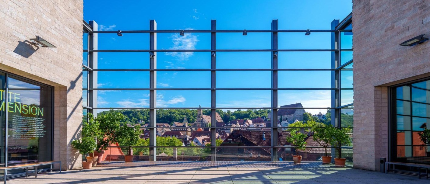 Blick von der Kunsthalle Würth in Schwäbisch Hall auf die Stadt durch eine große Glasfassade. Im Vordergrund stehen Pflanzen in Töpfen., © Michael Kühneisen Blick von der Kunsthalle Würth in Schwäbisch Hall auf die Stadt durch eine große Glasfassade. Im Vordergrund stehen Pflanzen in Töpfen., © Michael Kühneisen