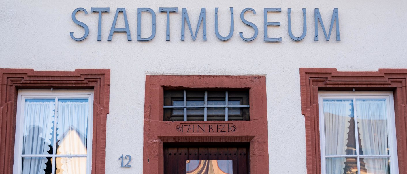 Fassade des Stadtmuseums mit dem Schriftzug 'STADTMUSEUM' &uuml;ber der T&uuml;r. Zwei Fenster mit Vorh&auml;ngen flankieren die T&uuml;r., &copy; Olivia + RichiPhotoart