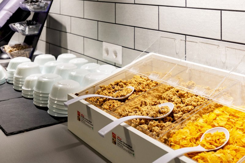 Frühstücksbuffet mit verschiedenen Müslisorten und Cornflakes in Behältern, weiße Schalen daneben gestapelt., © A&O Hostels Marketing GmbH