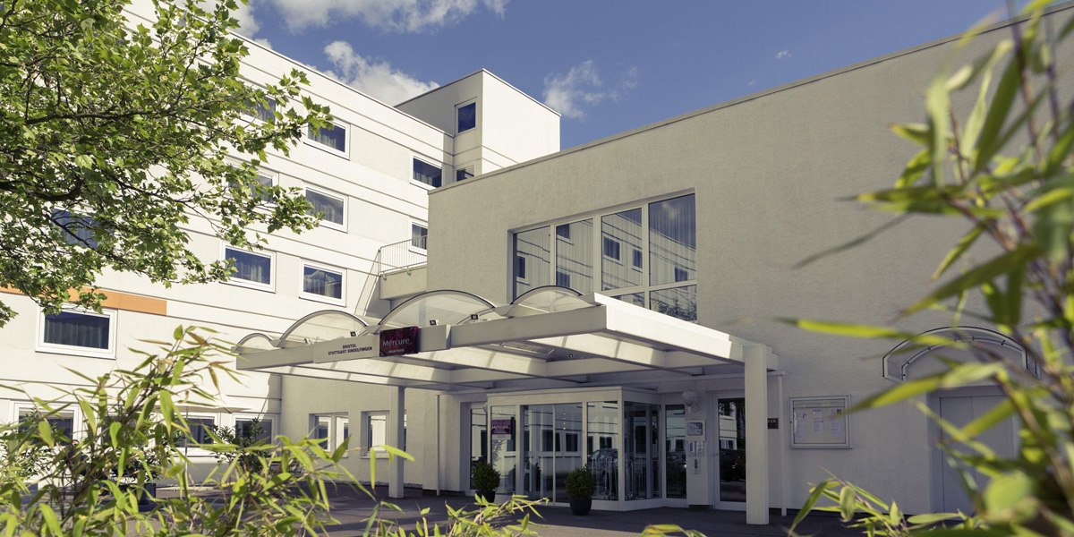 Modernes Gebäude mit Glasvordach, umgeben von Pflanzen. Der Himmel ist blau mit wenigen Wolken., © Mercure Bristol Stuttgart Sindelfingen