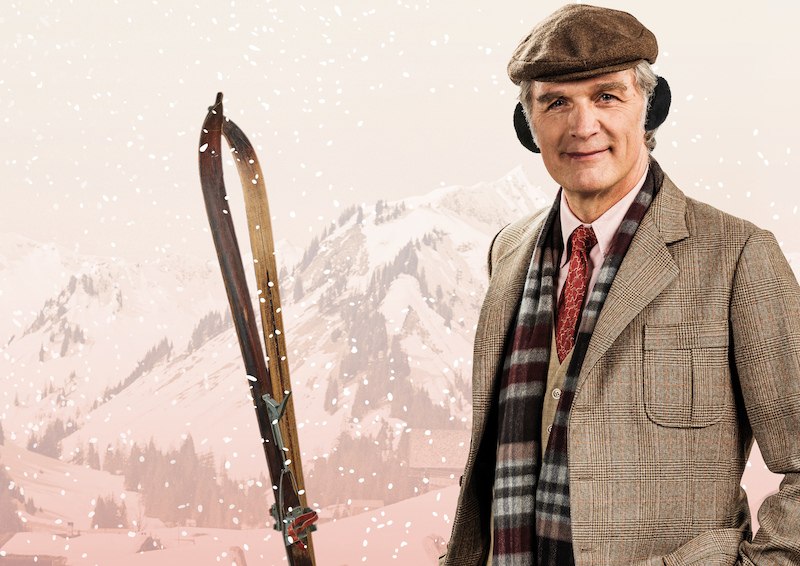 Ein Mann in Winterkleidung mit Mütze und Ohrenschützern steht vor schneebedeckten Bergen. Er hält Skier und trägt einen karierten Schal., © Stadt Leinfelden-Echterdingen, Kulturamt