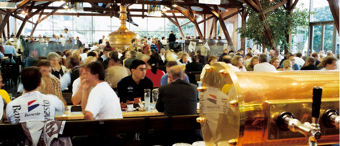 Ein belebtes Brauhaus mit vielen Menschen, die an Tischen sitzen. Im Hintergrund sind große Kupferkessel zu sehen., © Stuttgart-Marketing GmbH Ein belebtes Brauhaus mit vielen Menschen, die an Tischen sitzen. Im Hintergrund sind große Kupferkessel zu sehen., © Stuttgart-Marketing GmbH