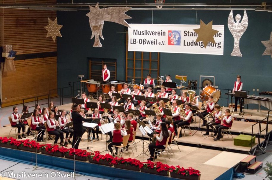 Ein Orchester in roten Westen spielt auf einer festlich dekorierten Bühne. Im Hintergrund ein Banner des Musikvereins LB-Oßweil e.V., © Musikverein Ludwigsburg-Oßweil e.V., Stadtkapelle Ludwigsburg