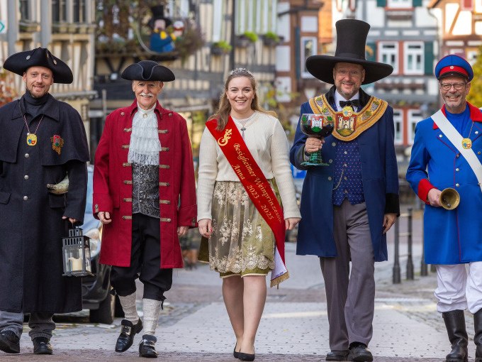 Fünf Personen in historischen Kostümen, darunter eine Frau mit Schärpe, gehen eine gepflasterte Straße entlang. Sie tragen Hüte und Mäntel., © Stadt Besigheim Fünf Personen in historischen Kostümen, darunter eine Frau mit Schärpe, gehen eine gepflasterte Straße entlang. Sie tragen Hüte und Mäntel., © Stadt Besigheim