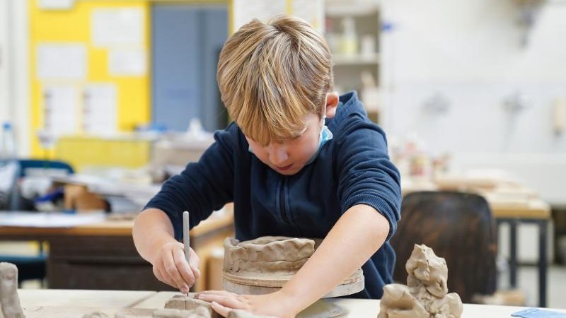Ein Junge arbeitet konzentriert an einer Tonfigur in einem Workshop. Er trägt einen blauen Pullover und sitzt an einem Tisch mit Tonmaterialien., © Kunstschule Labyrinth