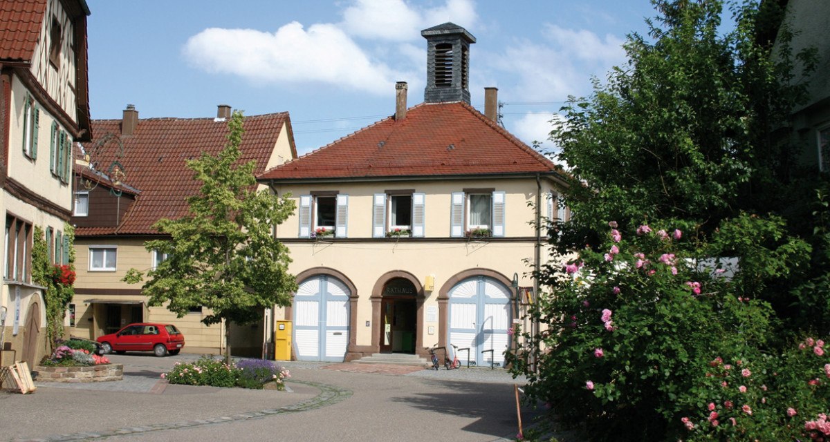 Das Rathaus in Ensingen mit rotem Ziegeldach und blauen Fensterläden, umgeben von blühenden Rosen und einem kleinen Platz., © Land der 1000 Hügel - Kraichgau-Stromberg Das Rathaus in Ensingen mit rotem Ziegeldach und blauen Fensterläden, umgeben von blühenden Rosen und einem kleinen Platz., © Land der 1000 Hügel - Kraichgau-Stromberg