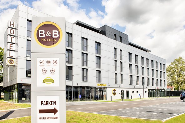 Moderne Außenansicht eines B&B Hotels mit großem Schild und Parkplatz für Hotelgäste. Der Himmel ist leicht bewölkt., © B&B Hotel Stuttgart-Neckarhafen