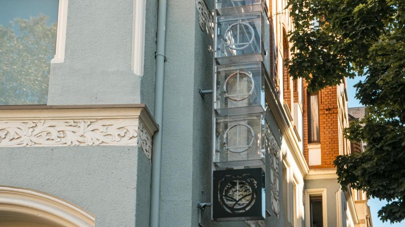 Fassade eines Gebäudes mit verzierten Elementen und einem Schild mit Logo. Ein Baum wirft Schatten auf die Wand. Klare, sonnige Atmosphäre., © SMG, Sarah Schmid Fassade eines Gebäudes mit verzierten Elementen und einem Schild mit Logo. Ein Baum wirft Schatten auf die Wand. Klare, sonnige Atmosphäre., © SMG, Sarah Schmid