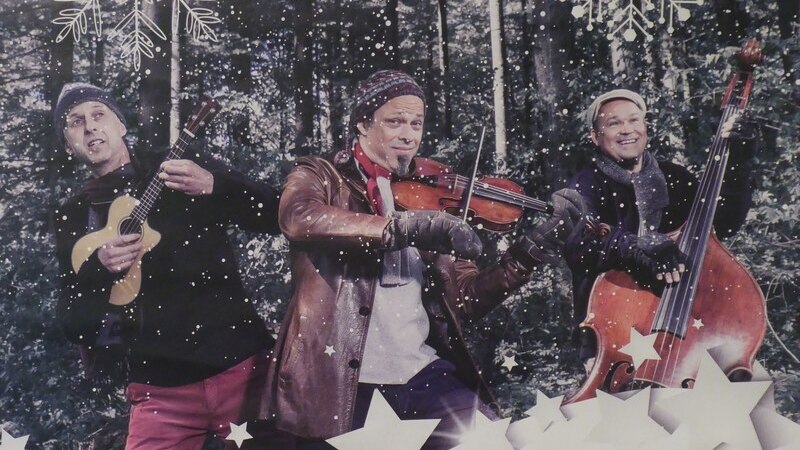 Drei Musiker im Wald, umgeben von Schneeflocken und Sternen, spielen Ukulele, Geige und Kontrabass. Winterliche Atmosphäre., © Mauerwerk GmbH