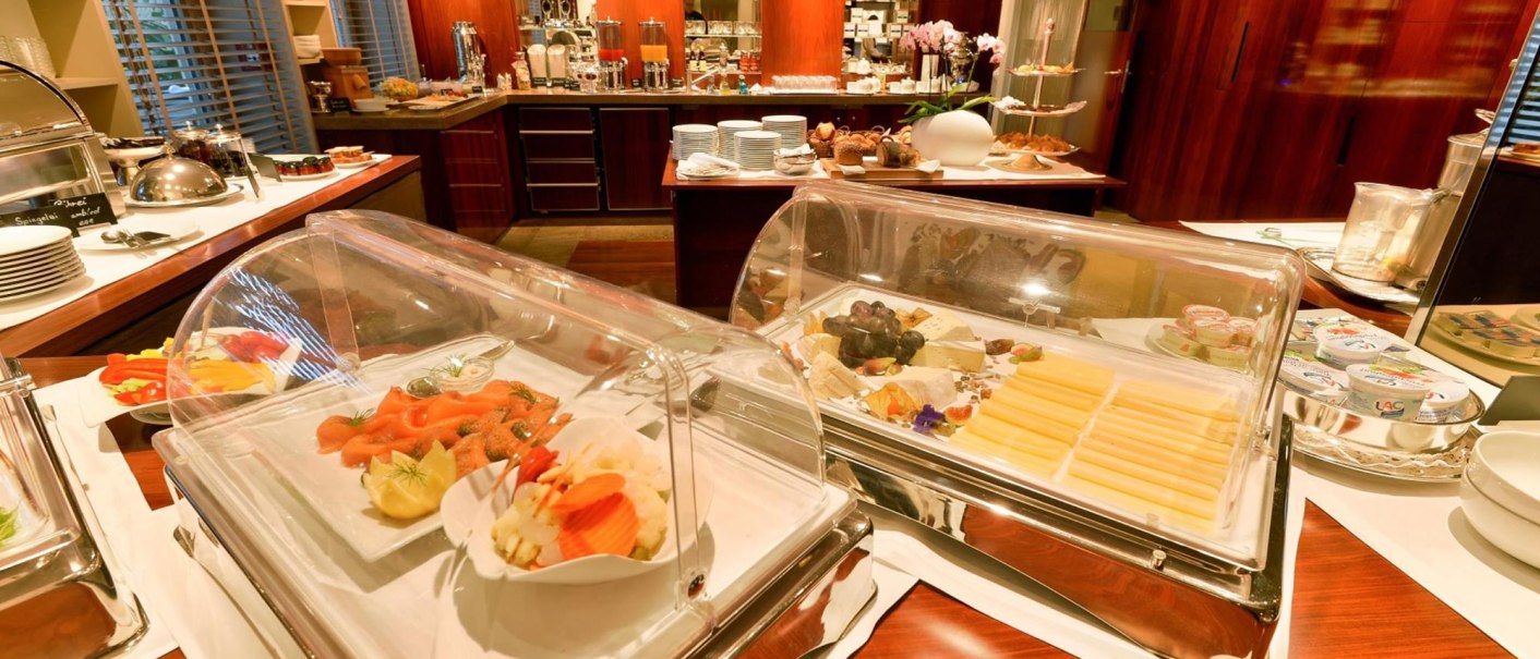 Ein elegantes Frühstücksbuffet mit Lachs, Käse und Gebäck in einem stilvollen Raum mit Holzverkleidung., © Ringhotel Adler Asperg