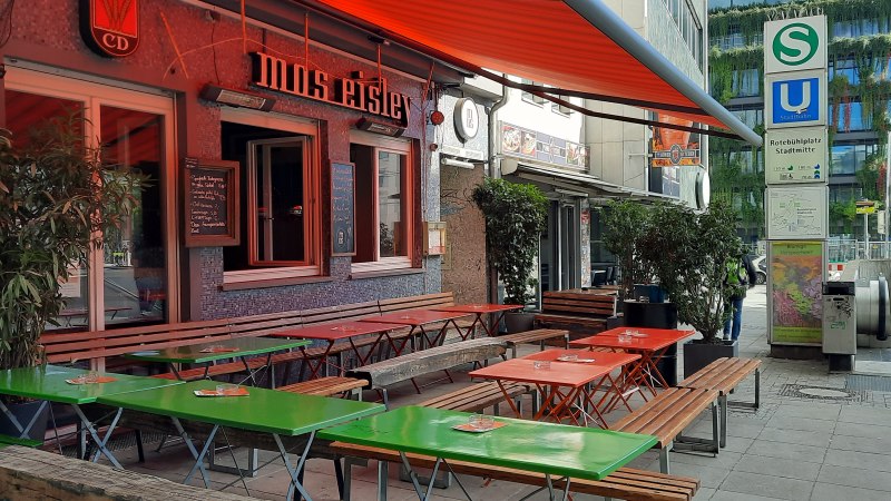 Außenbereich eines Cafés namens Mos Eisley mit bunten Tischen und Bänken. Daneben ein S- und U-Bahn-Schild am Rotebühlplatz Stadtmitte., © SMG Außenbereich eines Cafés namens Mos Eisley mit bunten Tischen und Bänken. Daneben ein S- und U-Bahn-Schild am Rotebühlplatz Stadtmitte., © SMG