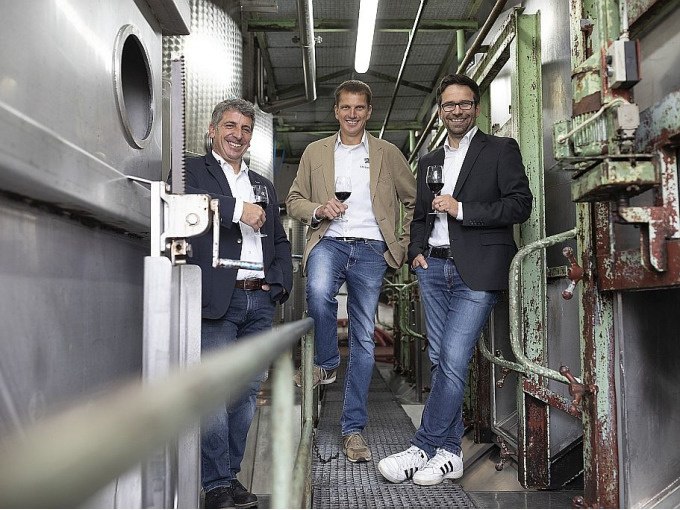 Drei Männer stehen in einer Weinkelterei, lächelnd mit Weingläsern in der Hand. Sie tragen legere, aber schicke Kleidung., © Esslinger Stadtmarketing &amp; Tourismus GmbH