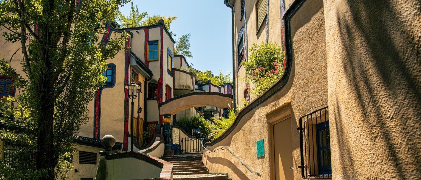 Das Hundertwasserhaus in Plochingen zeigt seine charakteristische bunte und wellenf&ouml;rmige Architektur, umgeben von Pflanzen und geschwungenen Linien., &copy; Stuttgart-Marketing GmbH, Sarah Schmid
