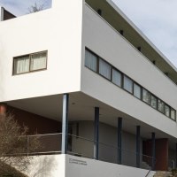Modernes Gebäude mit weißer Fassade und großen Fenstern, umgeben von Bäumen und einem Plakatständer., © Stuttgart Marketing GmbH, Sarah Schmid