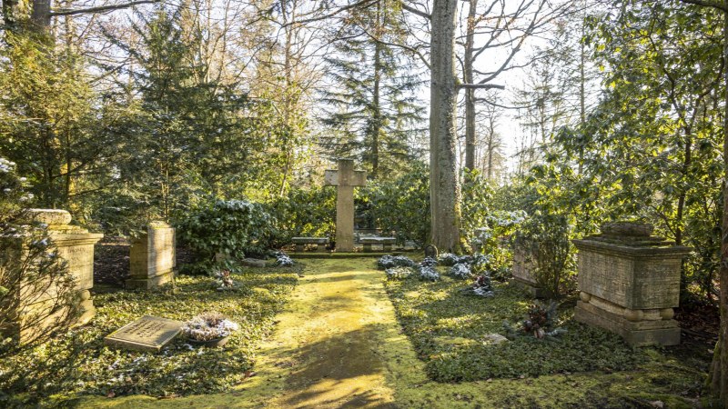 Ein ruhiger Friedhof mit einem großen Kreuz in der Mitte, umgeben von Bäumen und grüner Vegetation. Sonnenlicht fällt durch die Blätter., © Stuttgart-Marketing GmbH, Sarah Schmid Ein ruhiger Friedhof mit einem großen Kreuz in der Mitte, umgeben von Bäumen und grüner Vegetation. Sonnenlicht fällt durch die Blätter., © Stuttgart-Marketing GmbH, Sarah Schmid