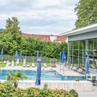 Ein Reha-Zentrum mit Pool, Liegestühlen und blauen Sonnenschirmen. Im Hintergrund sind Bäume und Gebäude zu sehen., © Christophsbad Klinikgruppe Ein Reha-Zentrum mit Pool, Liegestühlen und blauen Sonnenschirmen. Im Hintergrund sind Bäume und Gebäude zu sehen., © Christophsbad Klinikgruppe