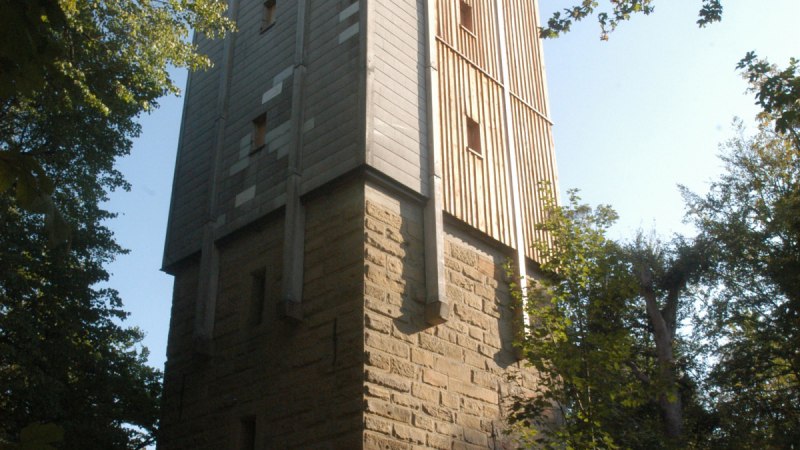 Ein hoher Turm aus Stein und Holz steht im Wald, umgeben von B&auml;umen. Der Himmel ist klar und sonnig., &copy; TGMB Marbach